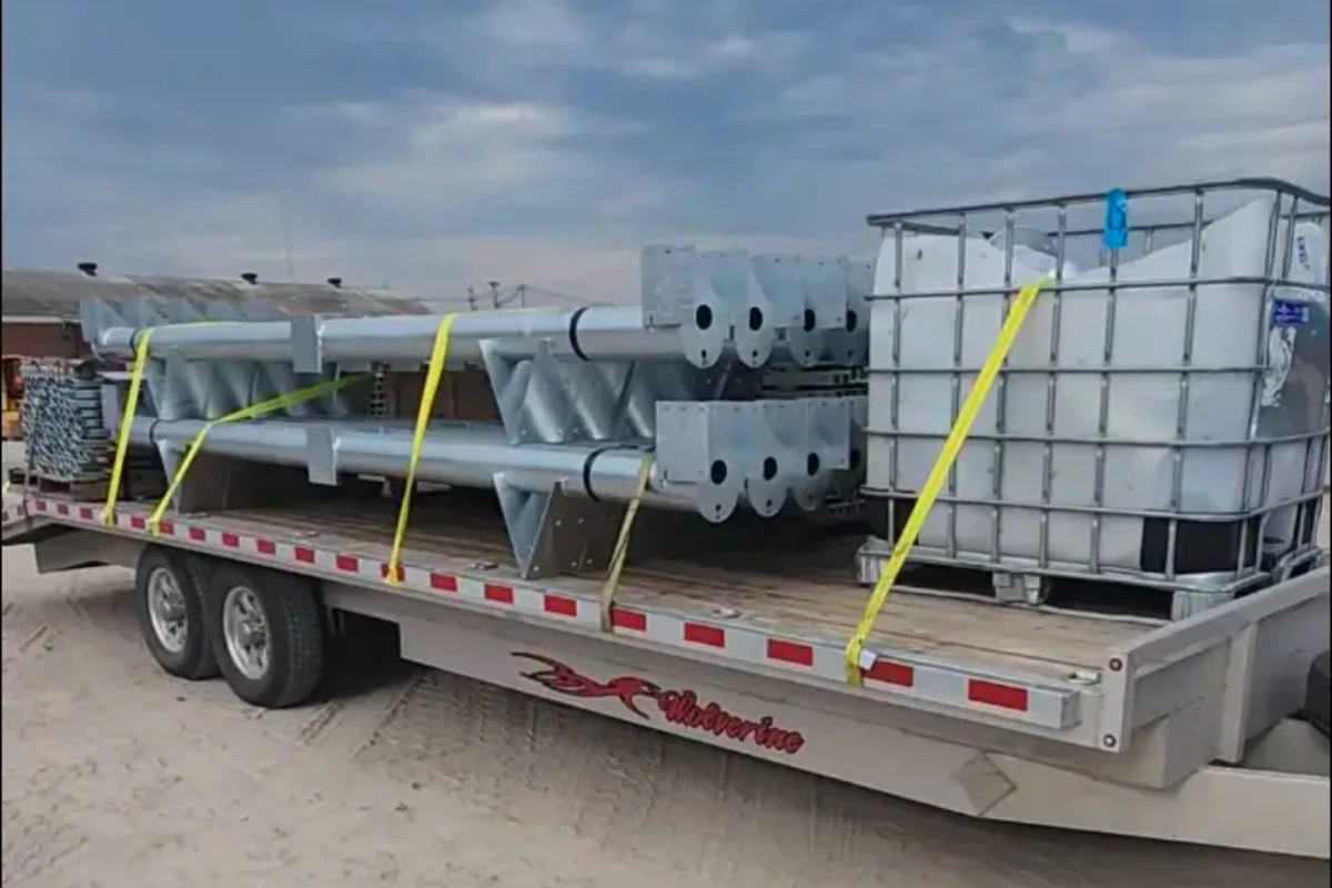 Flatbed trailer loaded with center pivot pipe spans, strapped for transport